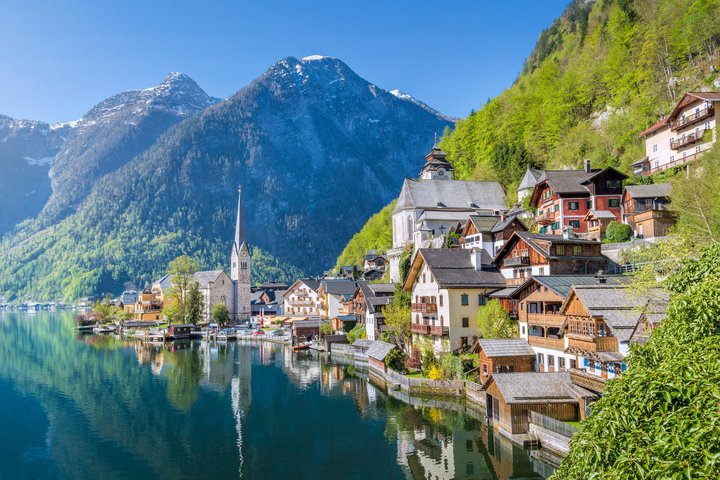 Een pittoresk uitzicht op Hallstatt in Oostenrijk, met kleurrijke huizen langs de oever van een helder bergmeer, omringd door indrukwekkende Alpenbergen en weerspiegeld in het kalme water.