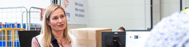 Warehouse manager speaking with a colleague at a workstation in a logistics facility.