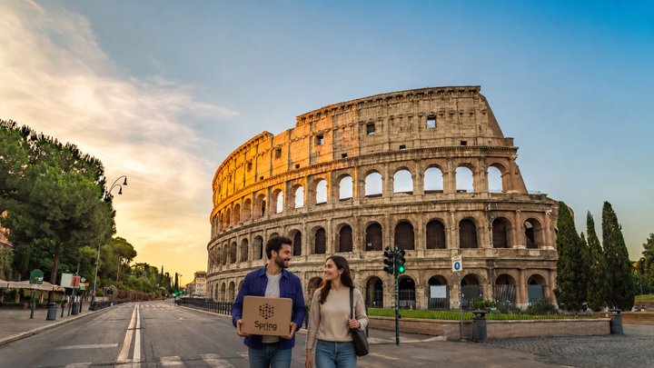 Due giovani con un pacco in mano camminano davanti al Colosseo.