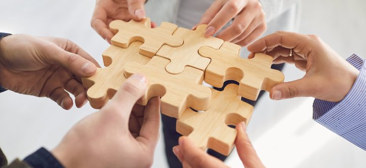 Many hands putting together a big wooden puzzle illustrating how easy the connection between Spring GDS and Woocmmerce can be