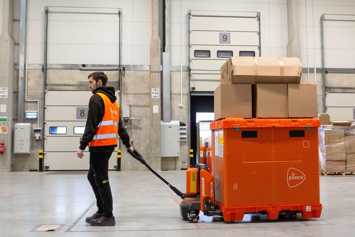 Warehouse worker pulling a pallet jack with a large container of parcels in a distribution centre.