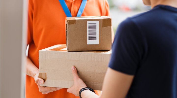 Close-up of a delivery person handing two cardboard packages to a recipient at the door.