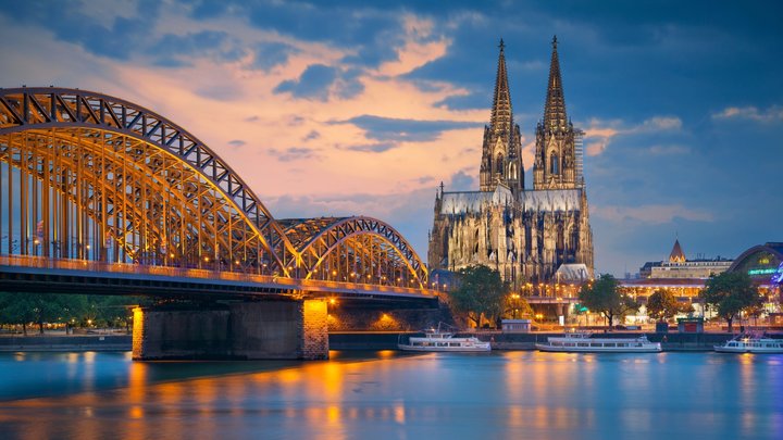 Blick auf den Kölner Dom mit Fluss und Brücke im Vordergrund.