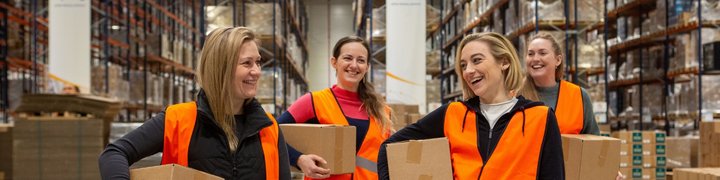 Quattro addetti al magazzino, con dei pacchi in mano, attraversano un centro logistico.