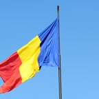 Romanian flag waving on a flagpole against a clear blue sky.