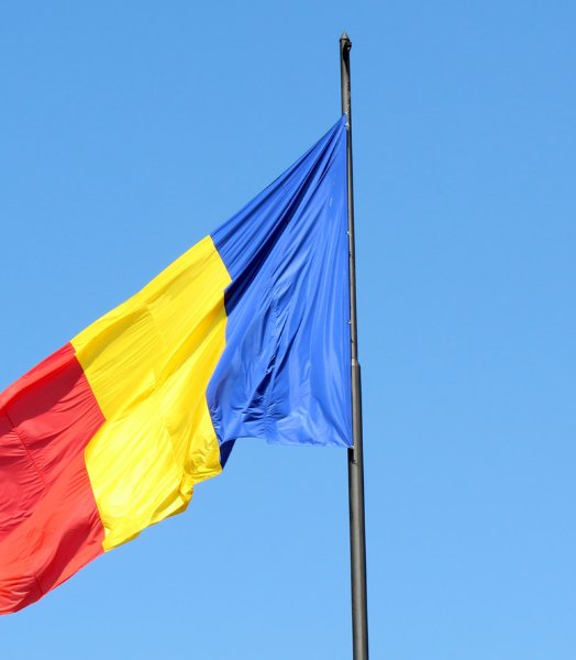Romanian flag waving on a flagpole against a clear blue sky.