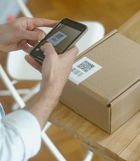 A person using a smartphone to scan a QR code on a cardboard delivery box.